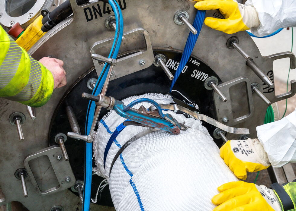 Ein Techniker mit gelben Schutzhandschuhen untersucht Rohre und Bauteile in einer Industrieanlage.