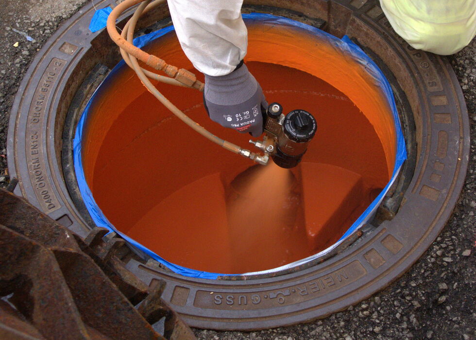 Ein Techniker steht über einem runden Tank und kontrolliert eine orange Flüssigkeit mit einem Messgerät/Absperrhahn.