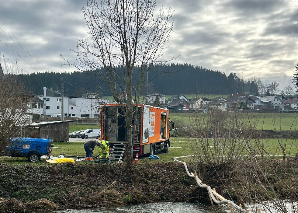 Arbeiter pflanzen an einem bewölkten Tag einen Baum am Bachrand nahe eines Dorfes.