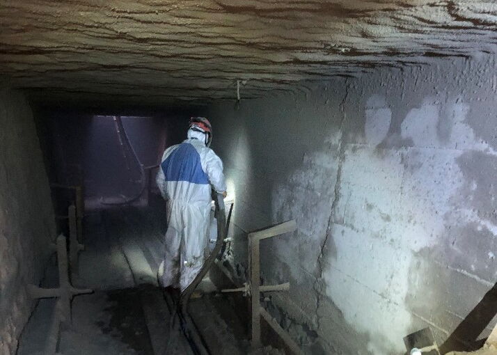 Person in Schutzkleidung geht durch einen schwach beleuchteten Bergwerksstollen mit technischer Ausrüstung