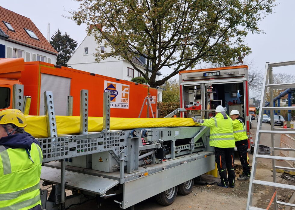 Personen in Warnkleidung laden Gerüstkomponenten von einem Lkw auf einer Wohnstraße ab.