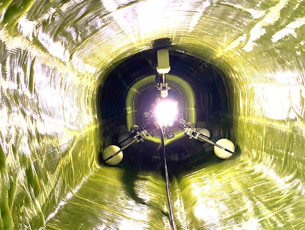 Blick in einen glänzenden gelb-grünen Industrietunnel mit einem Kabel, das zu einem hellen Licht führt.