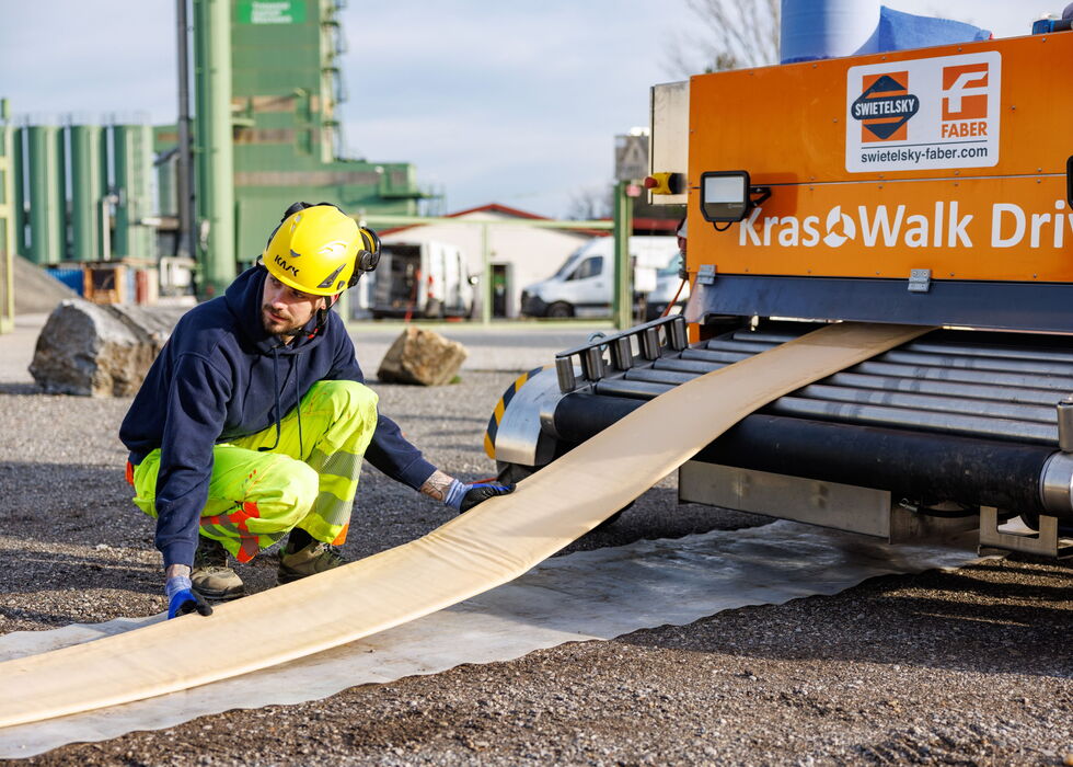 Zwei Bauarbeiter verlegen eine Asphaltbahn und bereiten die Fahrbahn auf einer Baustelle vor.