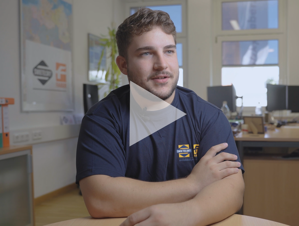 Ein junger Mann mit kurzem Haar und Bart sitzt an einem runden Tisch in einem Büro und scheint im Gespräch vertieft