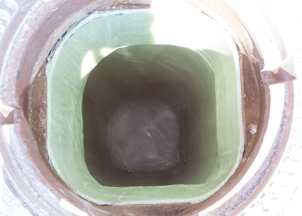 Blick von oben in einen runden Schacht mit grün ausgekleideter quadratischer Innenöffnung und dunkler Mitte.