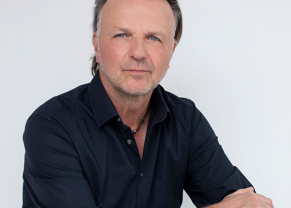 Porträt von Jörg Brunecker im dunklen Hemd vor hellem Hintergrund.