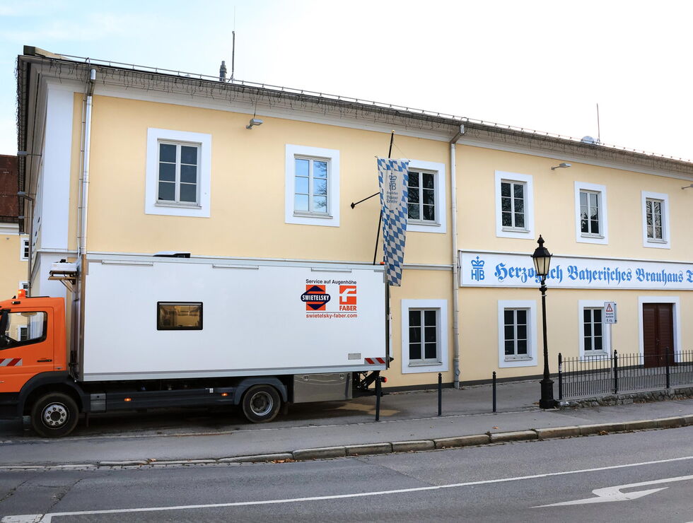 Ein orange-weißer Lieferwagen steht vor einem gelben Gebäude mit deutschem Schild.