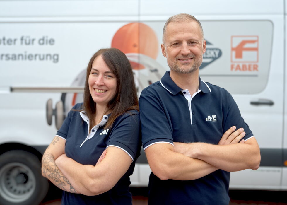 Two smiling company employees in navy polo shirts standing in front of a branded service van.