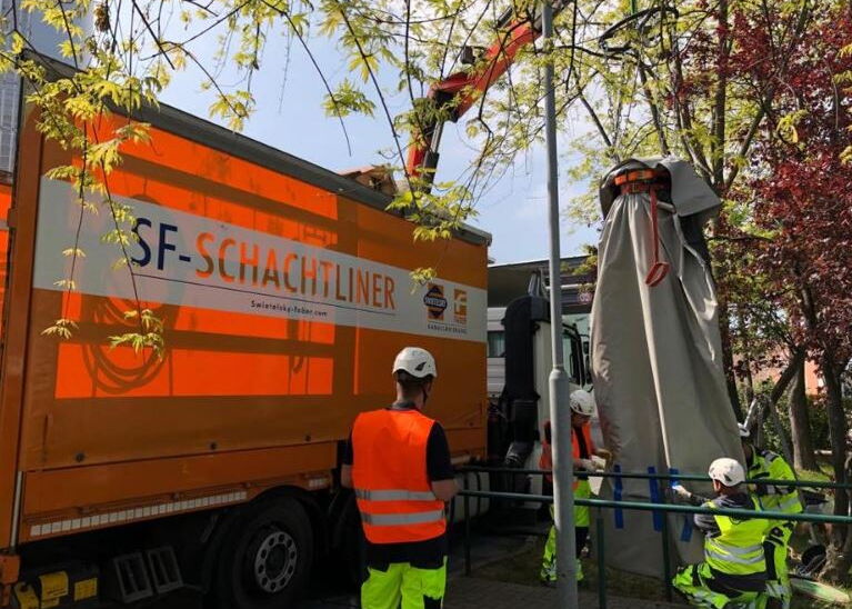Oranger Lkw von SF-Schachtlner und Arbeiter mit Warnwesten bei Arbeiten an Baumästen nahe einem Gebäude.
