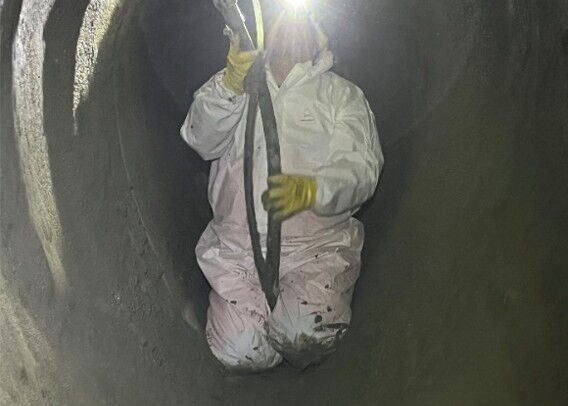 A worker in protective gear is kneeling in the storm sewer and spraying the GeoKrete mixed mortar