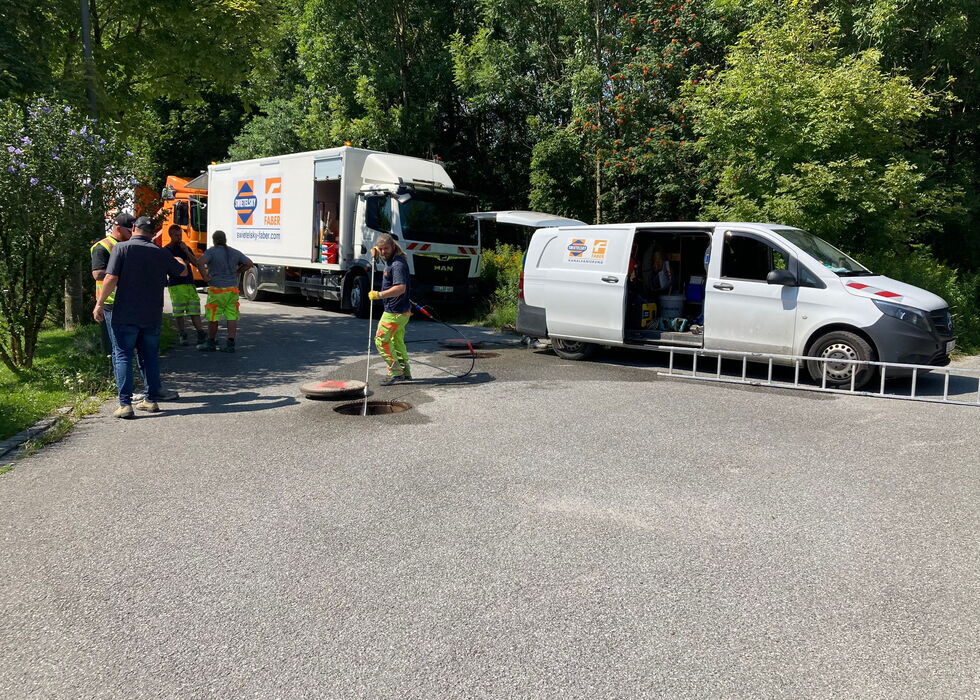 Arbeitskräfte und Einsatzfahrzeuge bei einem Vorfall am Straßenrand mit Kegeln und Ausrüstung auf einer baumgesäumten Straße.
