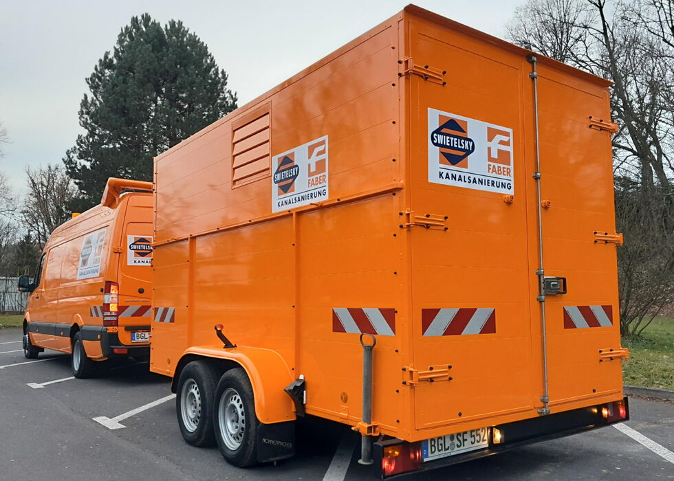 Zwei orange Entsorgungsfahrzeuge mit Kamerasammlung stehen auf einem Parkplatz.