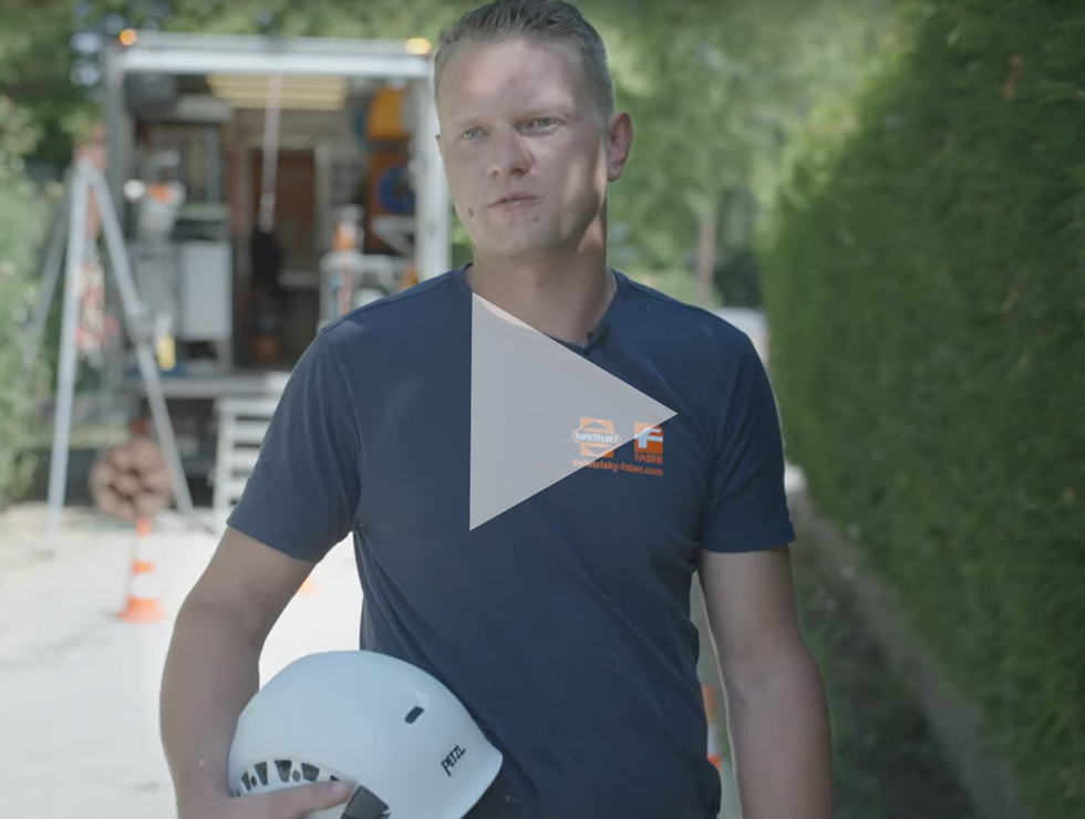 Mann in dunkelblauem Hemd hält weißen Schutzhelm, Baustelle und Warnschild im Hintergrund