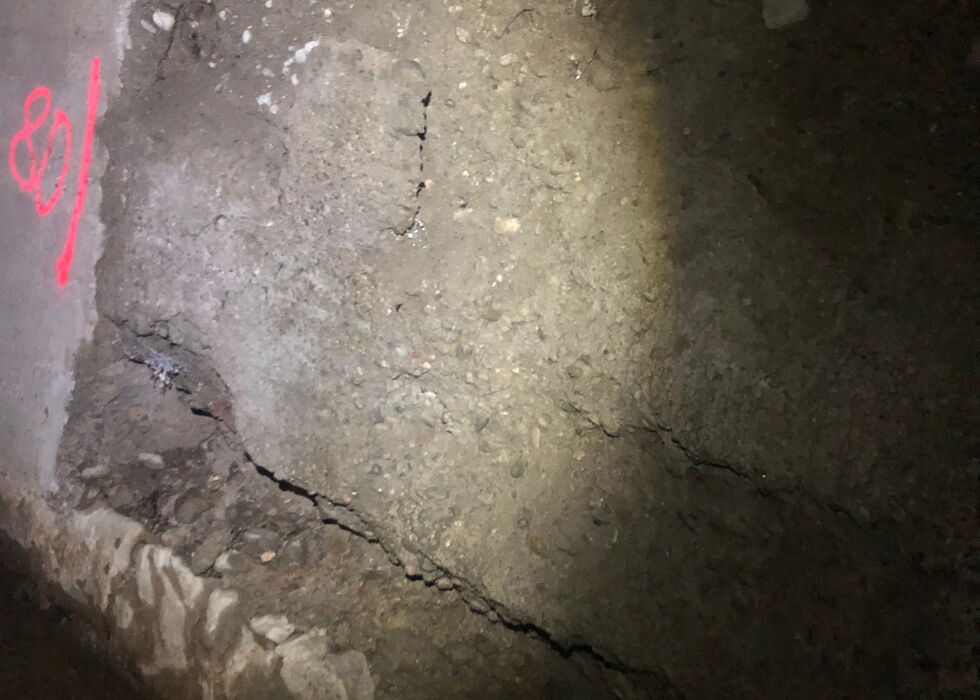 Nahaufnahme eines rissigen Betonbodens mit sichtbaren Schäden und Schutt bei schwachem Licht
