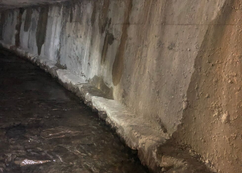 Geschwungener beschädigter Betonkanal unter der Erde mit fließendem Wasser