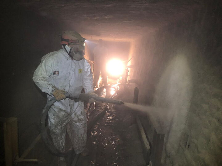Person in Schutzkleidung sprüht in einem schwach beleuchteten unterirdischen Tunnel