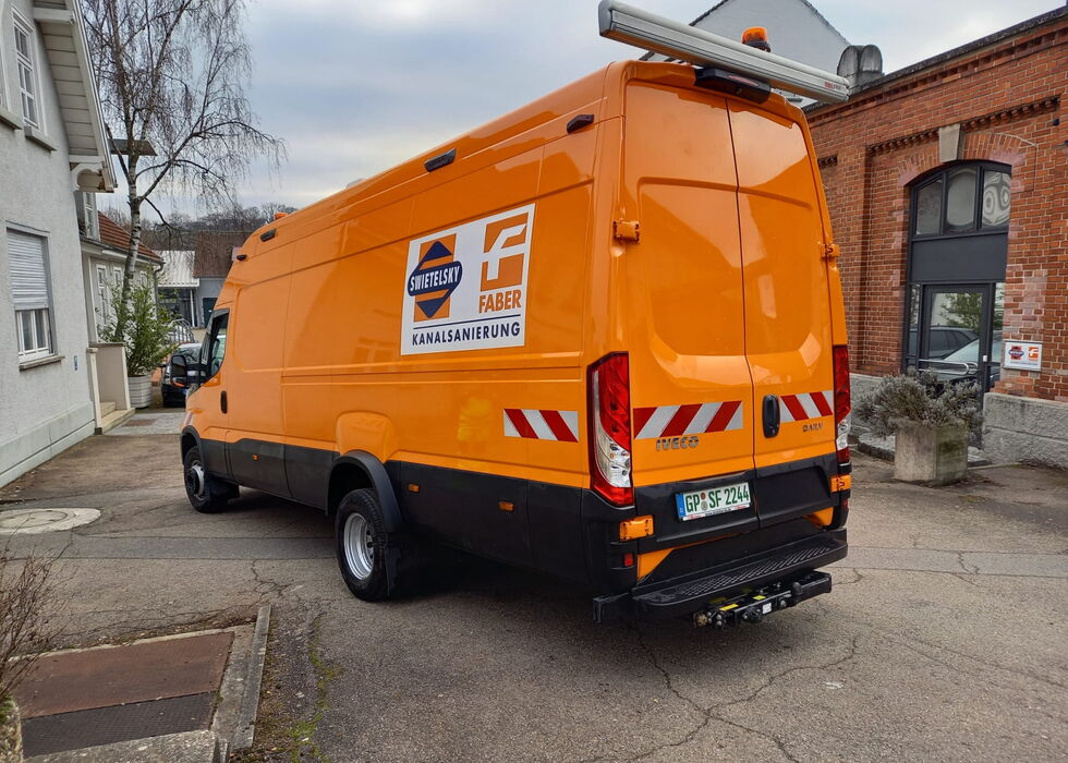 Oranger Servicewagen mit Firmenlogo steht neben Backsteingebäuden auf einem Hof.