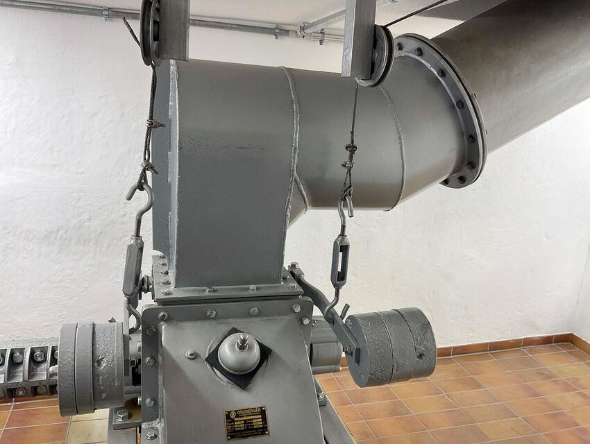 Nahaufnahme einer grauen Industriemaschine, die in einem gefliesten Raum mit großen Lüftungskanälen verbunden ist.