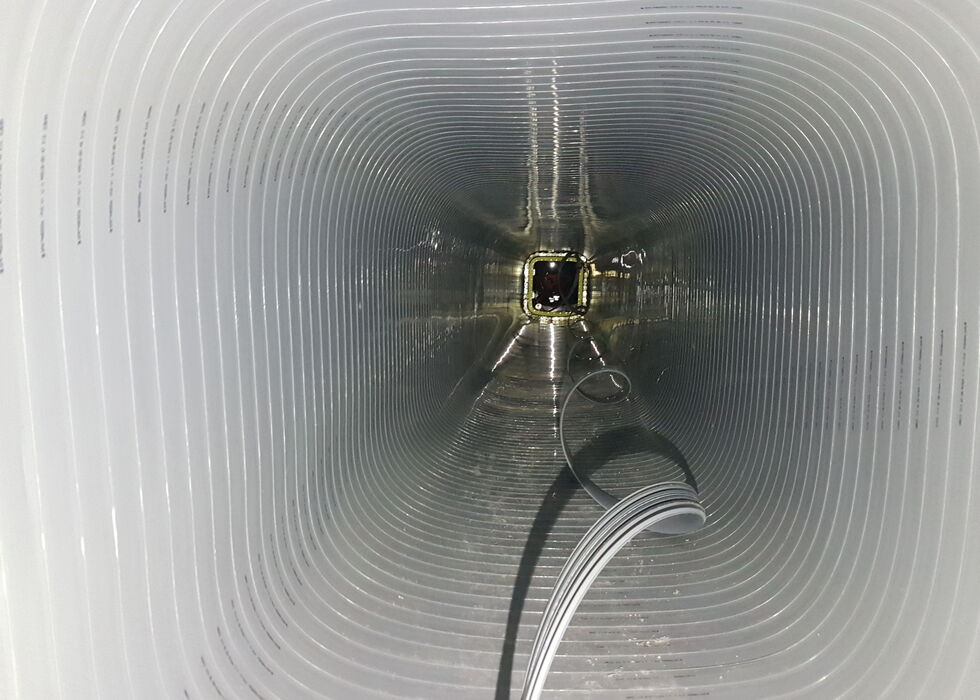 Blick in einen großen, gerippten Industrietunnel mit Kabeln am Boden, die zu einer entfernten Öffnung führen.