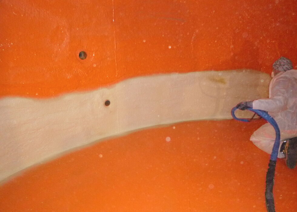Ein Arbeiter sprüht die dritte Lage der Beschichtung auf die Wand des Behälters.
