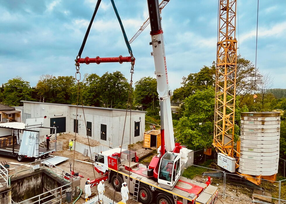 Mobilkran auf einer Baustelle hebt eine verpackte Palette neben einem teilweise errichteten Gebäude.