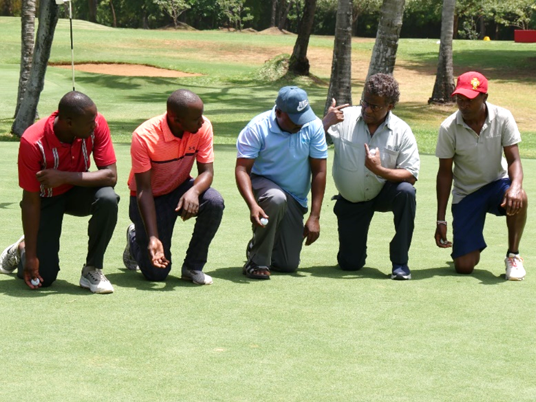 Fünf Männer knien auf dem Grün bei einer Golf-Putting-Übung im Freien.