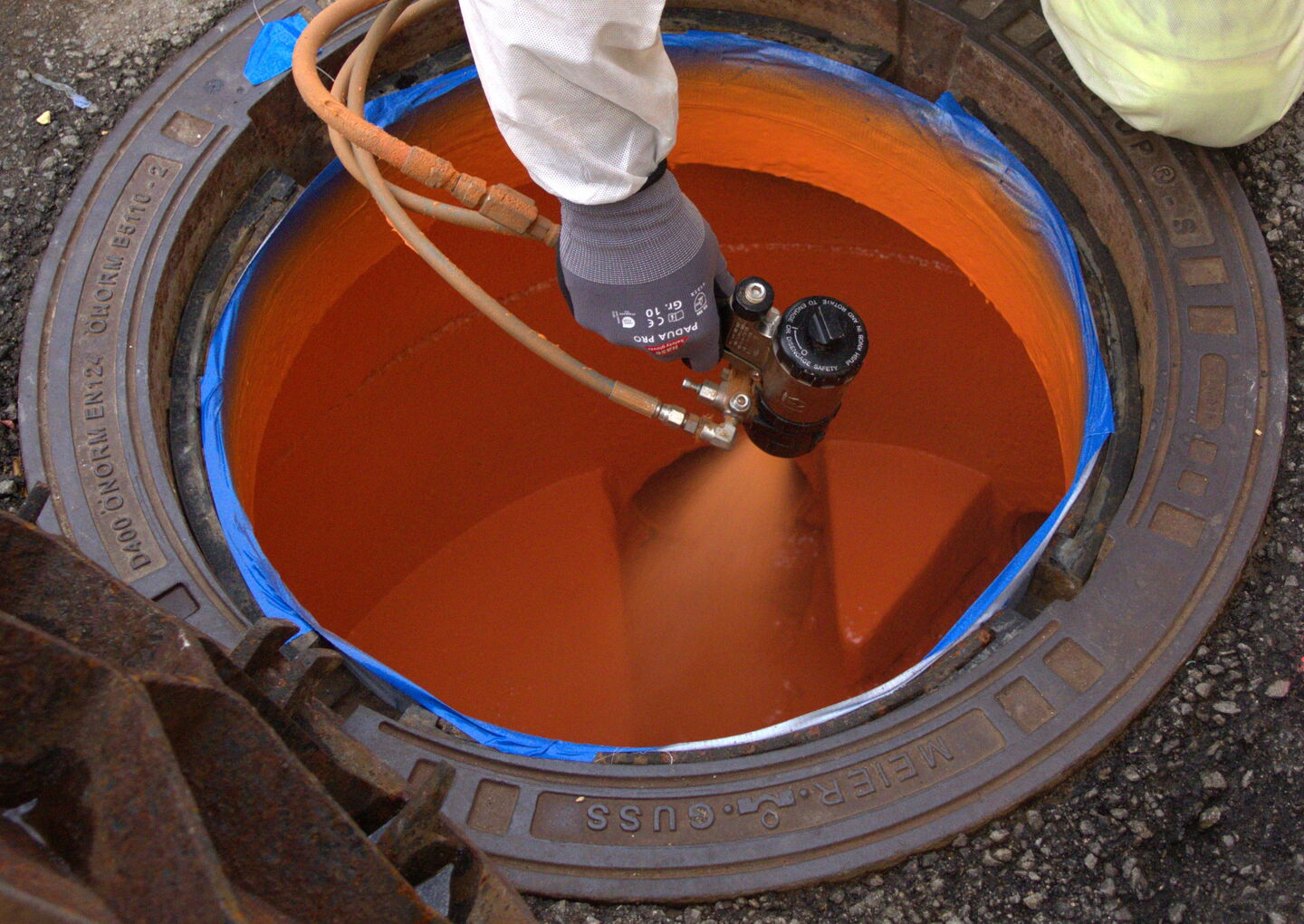 Ein Techniker steht über einem runden Tank und kontrolliert eine orange Flüssigkeit mit einem Messgerät/Absperrhahn.