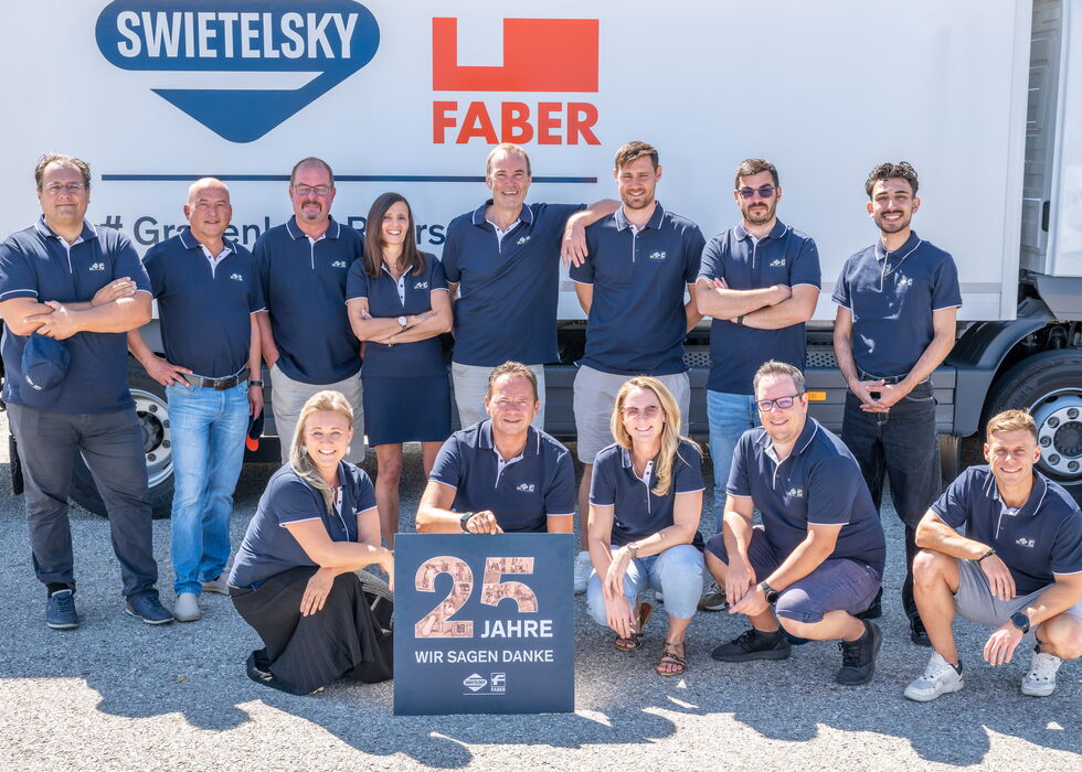 Team von Mitarbeitenden posiert vor einem Lkw und hält ein Schild zum 25-jährigen Jubiläum.