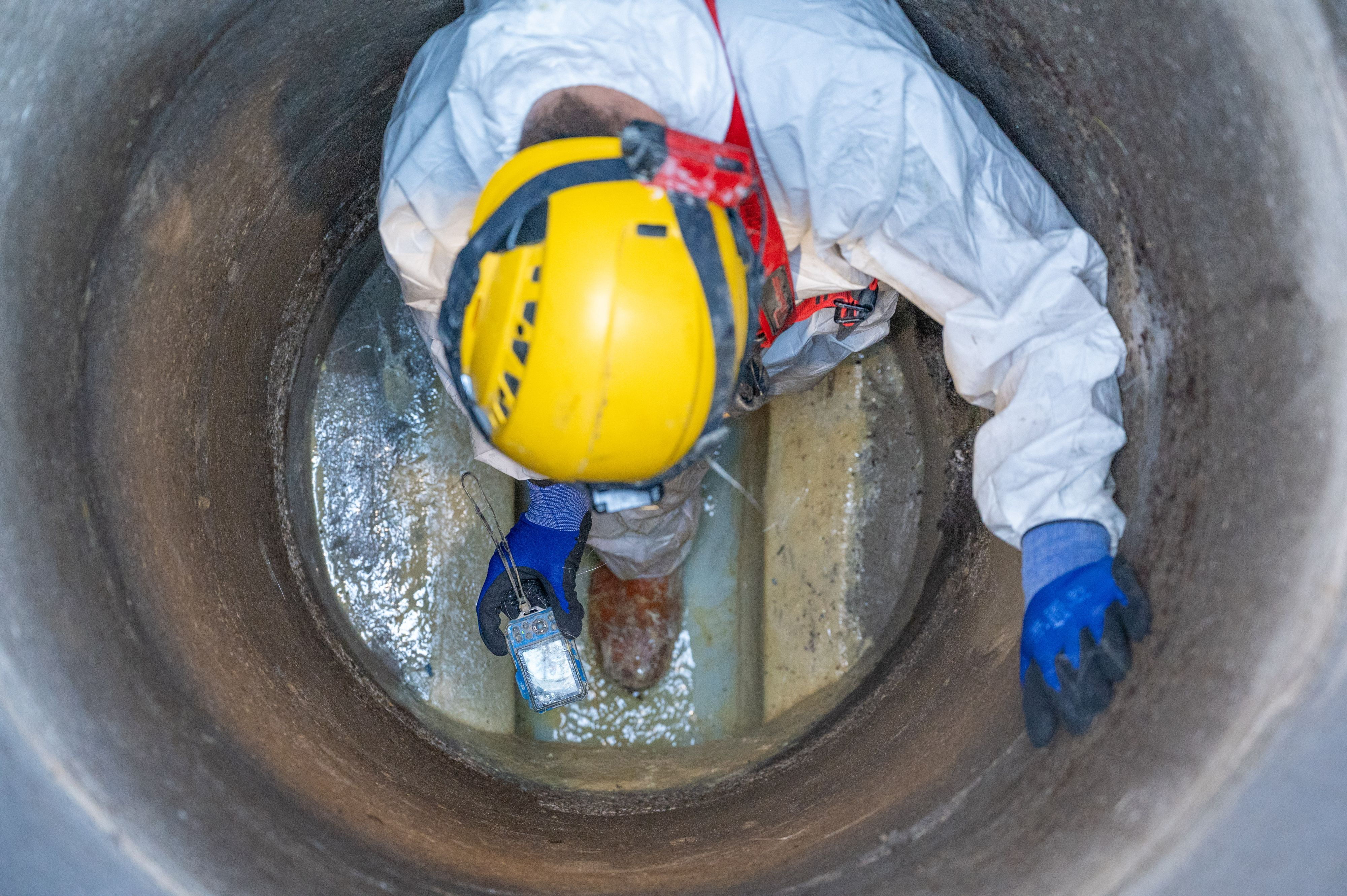 Ein Arbeiter in Schutzausrüstung kriecht in einem großen Abwasserrohr, um es zu inspizieren oder zu reparieren.