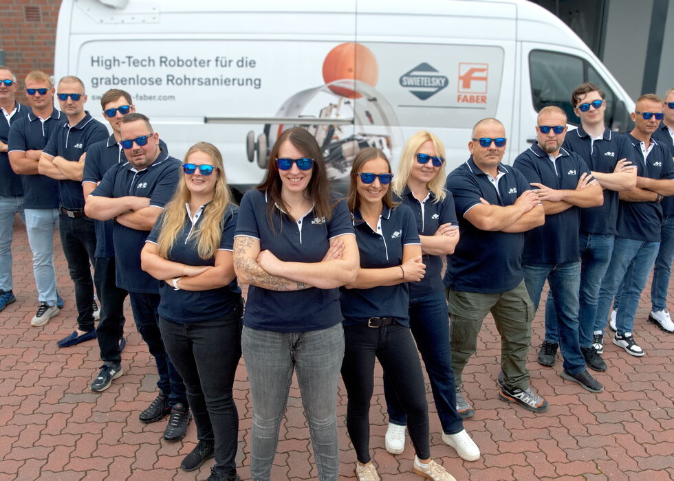 Group of staff in navy shirts and sunglasses standing with crossed arms in front of a branded van.