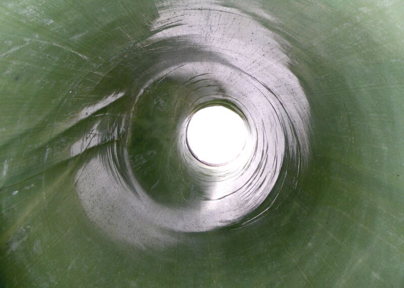 Blick durch das Innere eines grünen Tunnels auf eine helle, kreisförmige Öffnung.