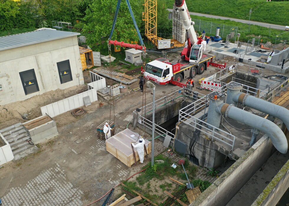 Luftaufnahme von Arbeitern und einem Kran auf einer Industriebaustelle mit Rohren und Betonstrukturen.