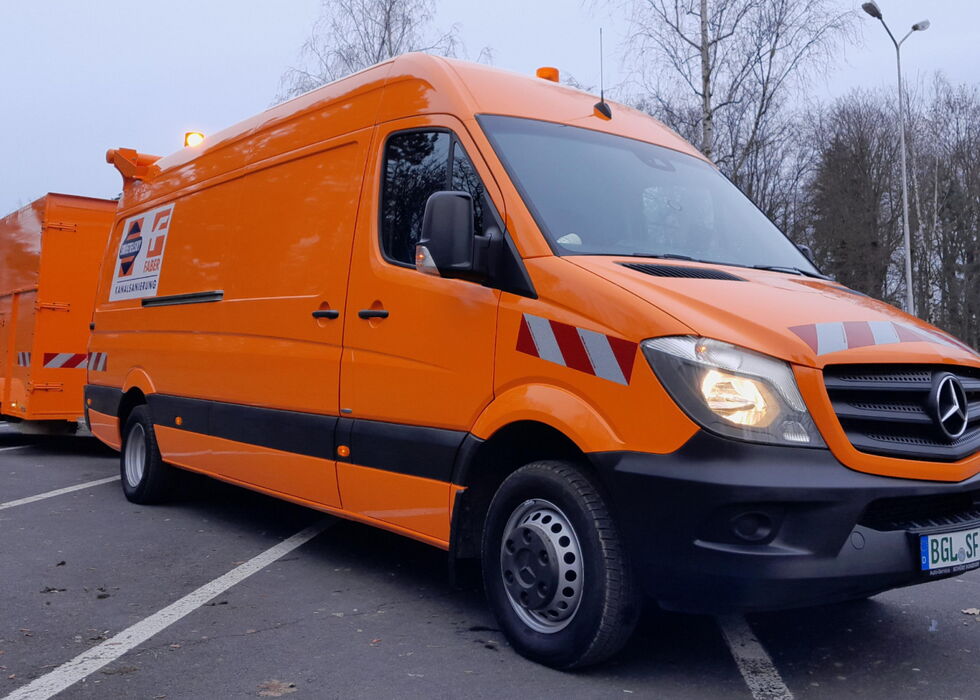 Oranger Mercedes-Nutzwagen mit passendem Anhänger am Straßenrand.