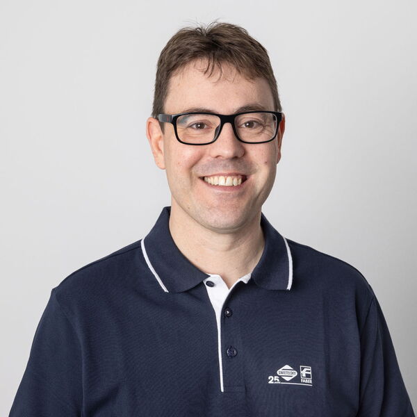 Lächelnder Mann mit Brille und dunkelblauem Poloshirt vor hellem Hintergrund.