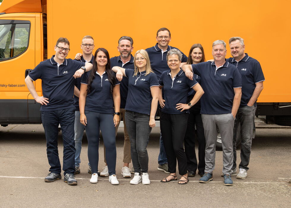 Gruppe von Mitarbeitern posiert gemeinsam vor einem orangefarbenen Lkw.