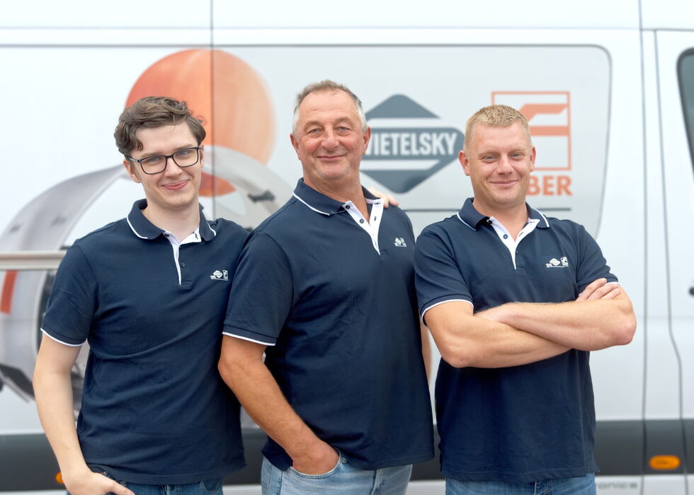 Three smiling men standing in front of a branded van, wearing navy polo shirts.