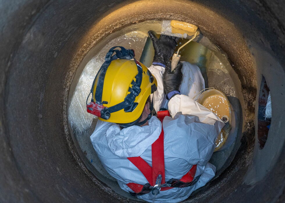 Arbeiter mit Schutzkleidung und Helm in einem engen Rohr oder Tunnel bei einer Inspektion.