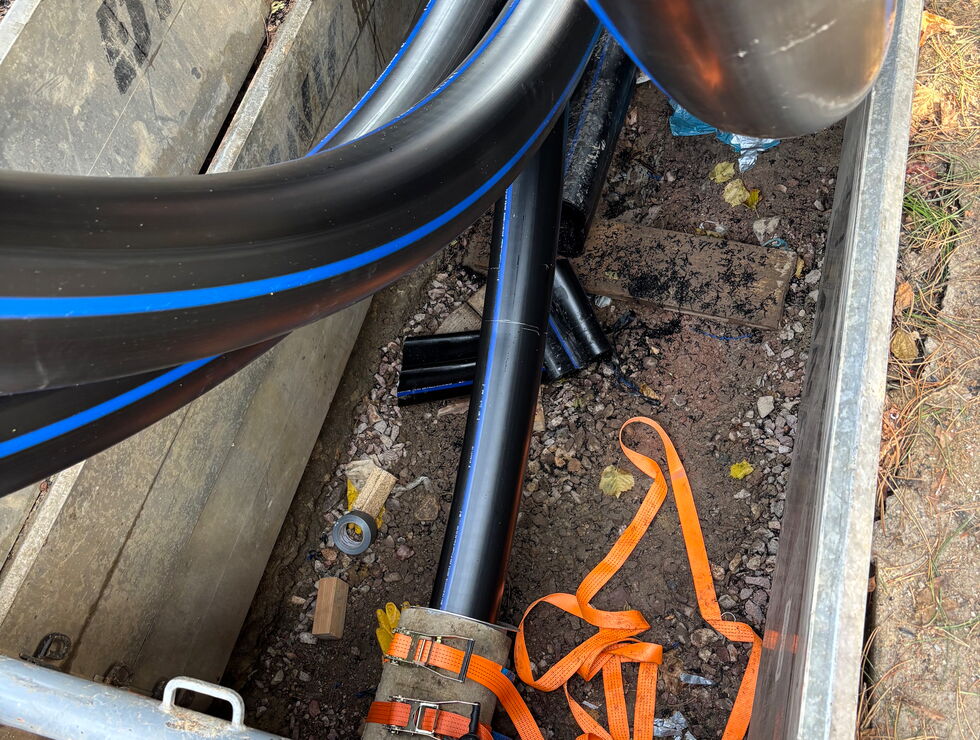 Schwarze Versorgungsleitungen liegen in einem Graben, mit orangefarbenen Gurten und Bauschutt.