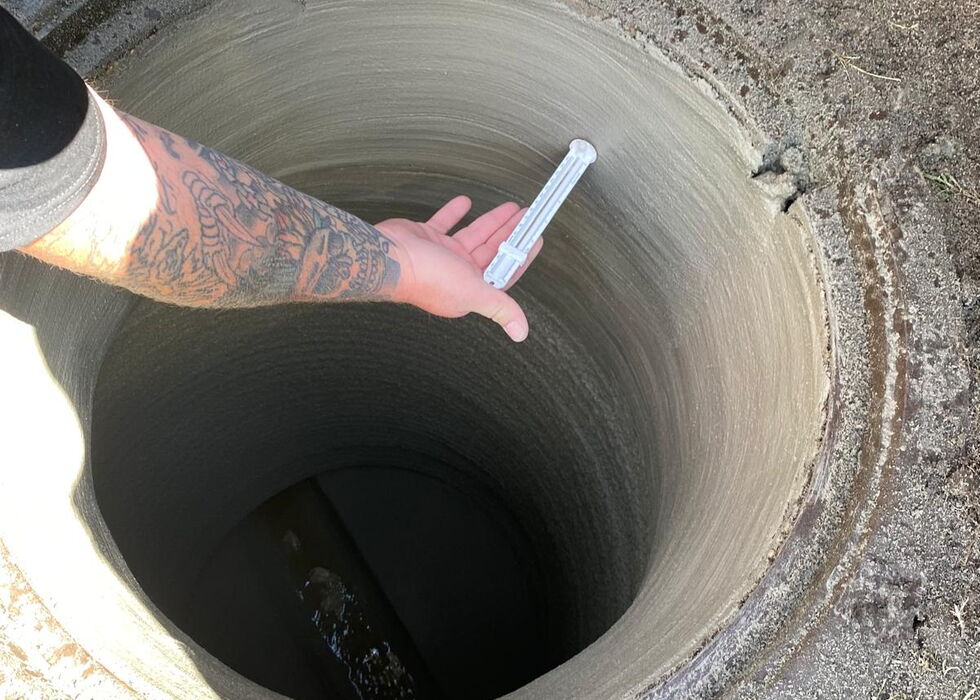 Eine Person lässt ein Maßband in einen tiefen, runden Brunnen im Freien hinab.
