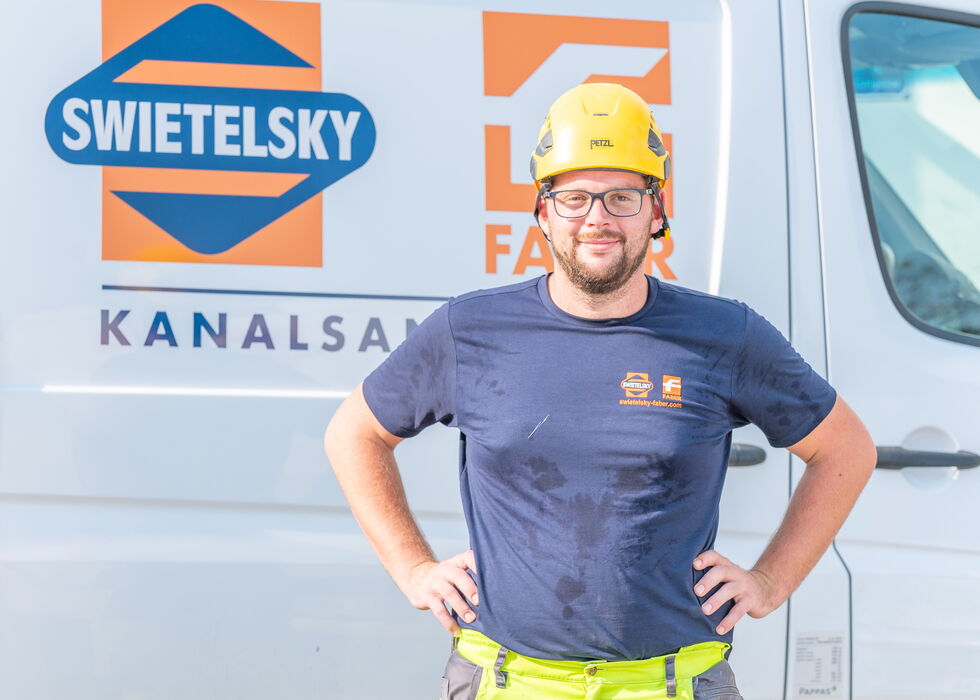 Ein Bauarbeiter mit Schutzhelm steht vor einem Swietelsky-Servicewagen.