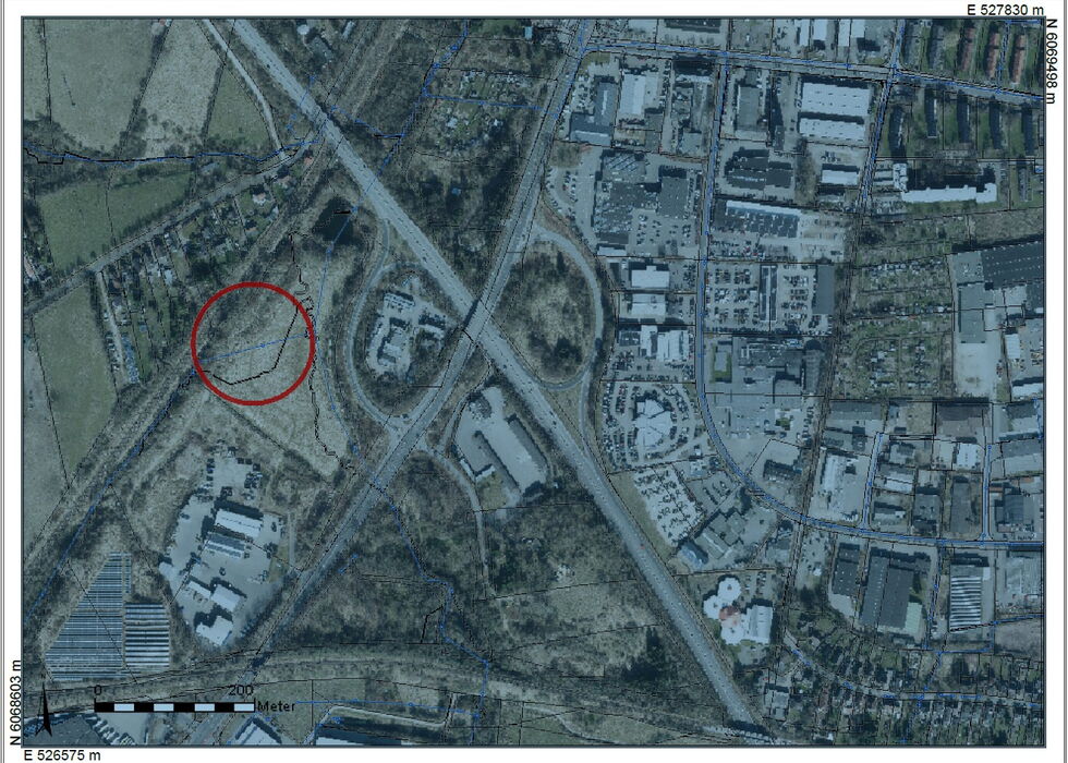 Satellitenbild eines Stadtgebiets mit rotem Kreis, der einen Ort nahe Straßen und Gebäuden markiert.