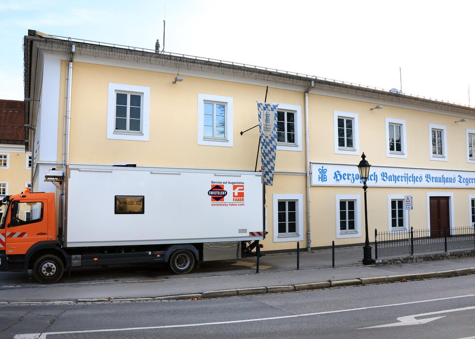 Ein orange-weißer Lieferwagen steht vor einem gelben Gebäude mit deutschem Schild.