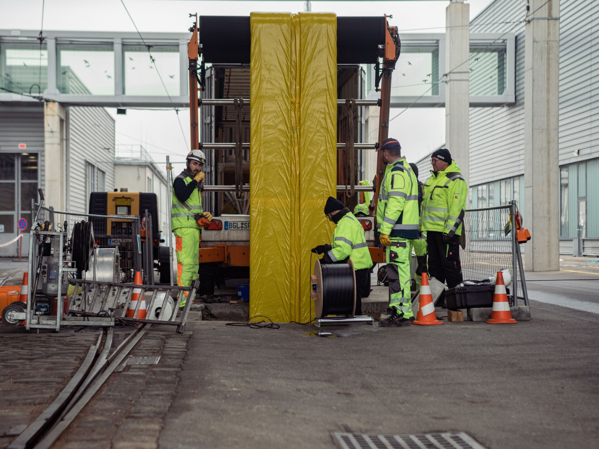 Arbeiter in Warnkleidung bedienen Geräte an einer abgedeckten Struktur auf einer Straßenbaustelle.