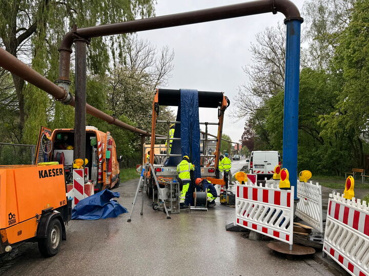 Arbeiter und Absperrungen um Maschinen bei der Reparatur einer Rohrleitungsquerung auf nasser Straße.