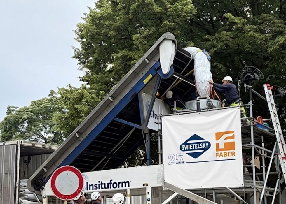 Lkw lädt Synthesefaserliners auf einer Baustelle mit Arbeitern, Absperrungen und Pylonen.