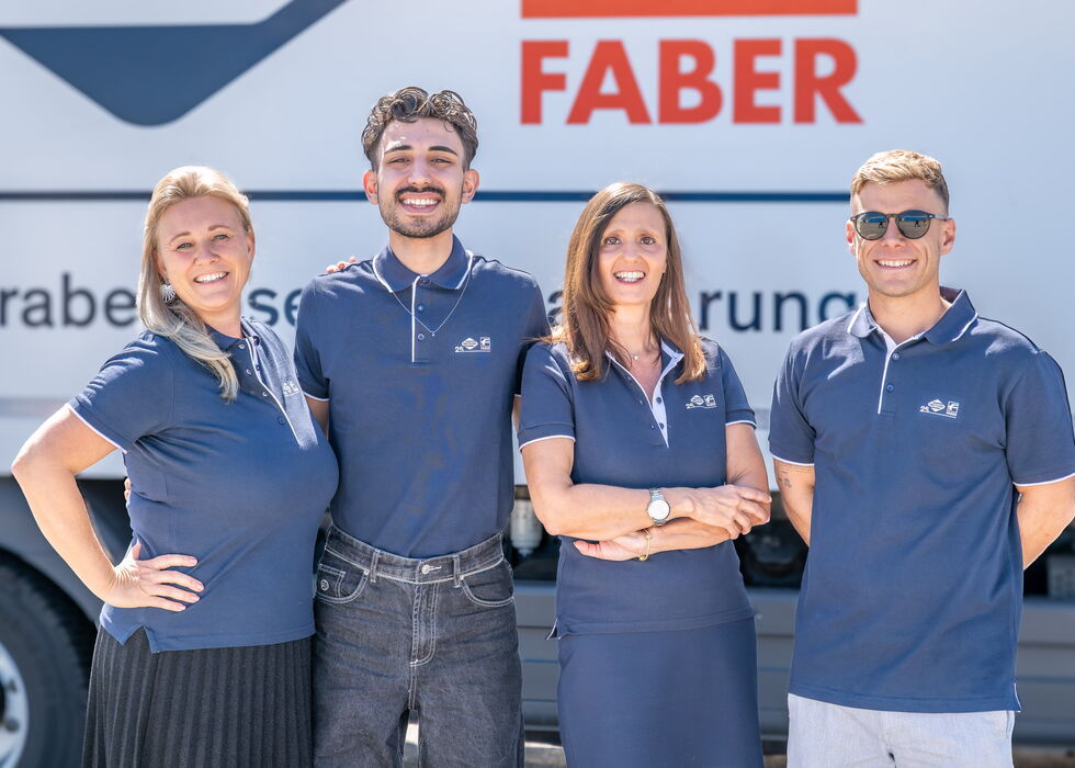 Vier lächelnde Mitarbeitende stehen gemeinsam vor einem Fahrzeug mit FABER-Logo.
