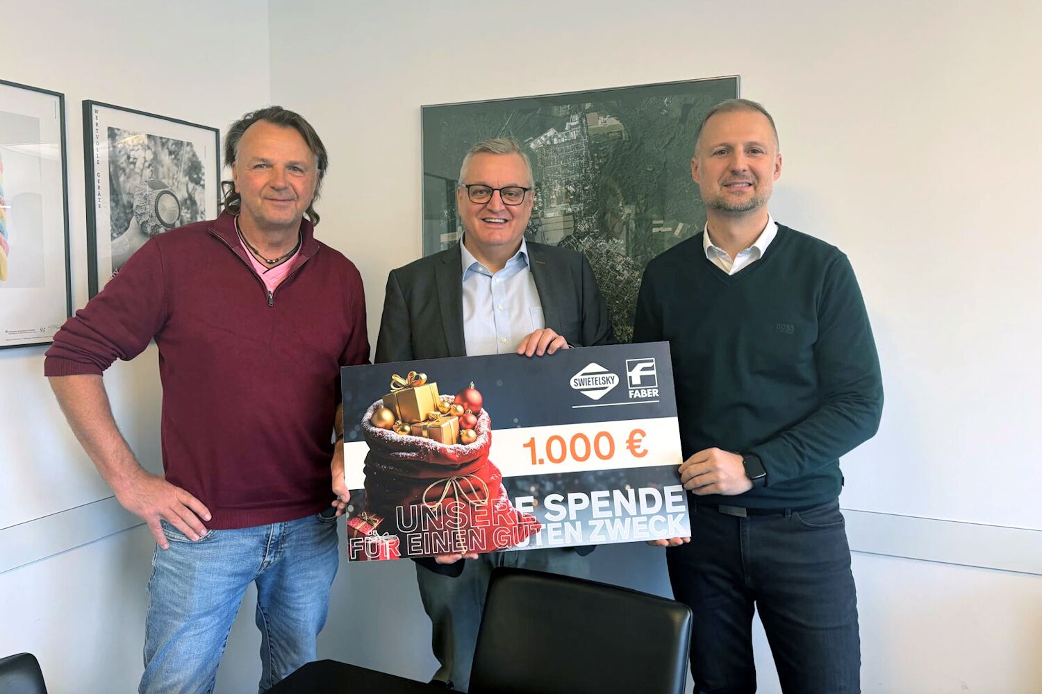Drei Männer stehen drinnen und halten gemeinsam einen großen Scheck über 1.000 Euro.