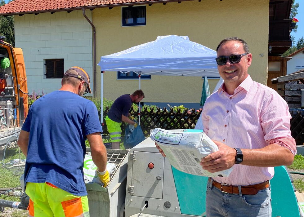 Zwei Männer verladen Gegenstände bei einer Veranstaltung im Freien neben einem Haus an einem sonnigen Tag.