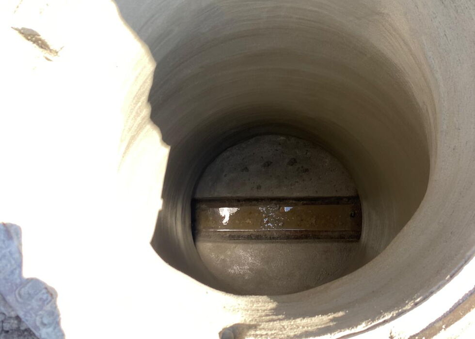 Blick von oben in einen tiefen Betonschacht mit etwas Wasser am Boden.