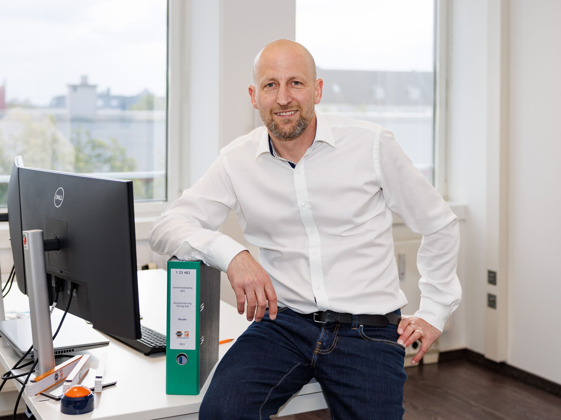 Der lächelnde Dipl.-Ing. Peter Prossliner sitzt in weißem Hemd an einem Schreibtisch neben einem Computer in einem hellen Büro.